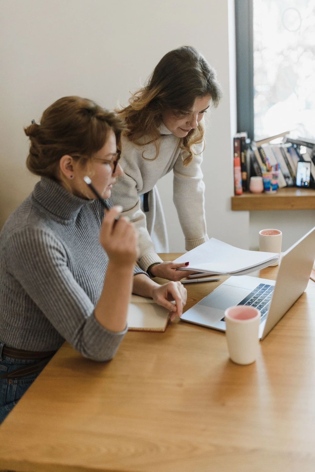Pay Solution – Lohn- und Gehaltsberatung – Dieses Bild zeigt zwei Kollegen, die an einem Holzschreibtisch in einem hell erleuchteten Arbeitsbereich an einem Laptop und Dokumenten zusammenarbeiten. Pay Solution – Lohn- und Gehaltsberatung –